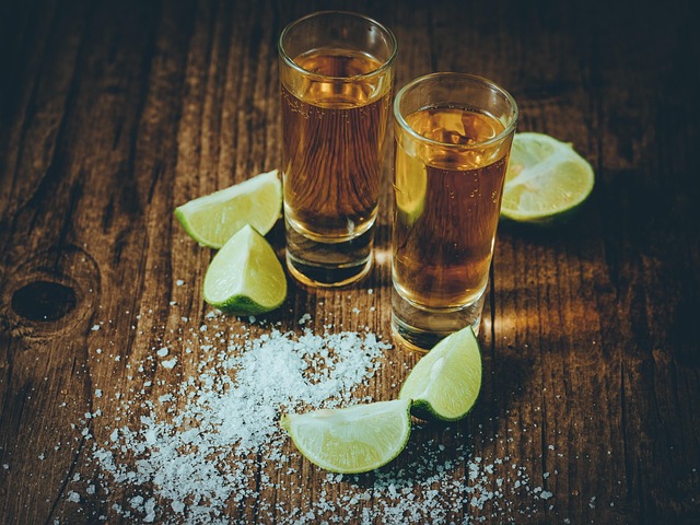 Two shot glasses with amber liquor, lime wedges, and scattered salt