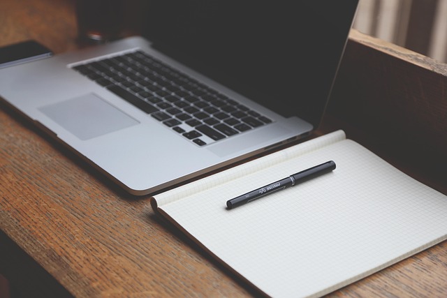 A laptop, notebook, and pen on a wooden desk