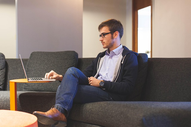 A man sitting on a couch working on a laptop computer