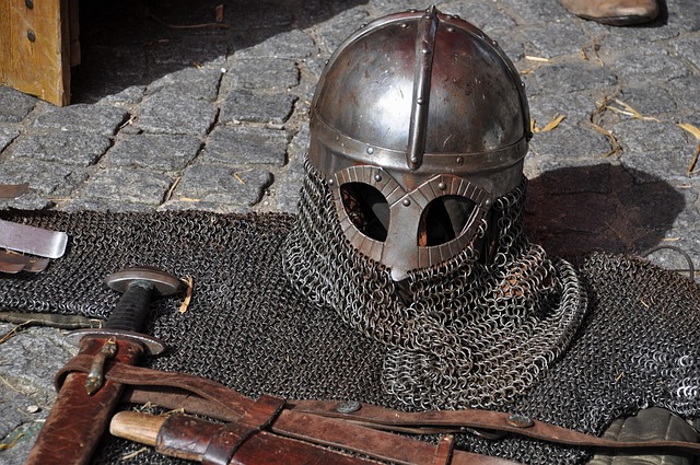 A medieval helmet, chainmail coif, and a sword resting on cobblestones