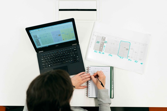 Top-down view of a person writing in a notebook next to a laptop