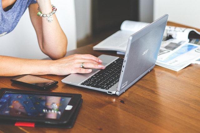A person using a laptop on a wooden desk with devices
