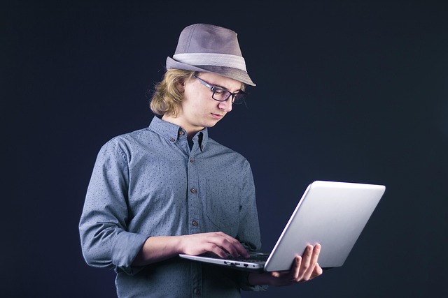 A young man wearing a hat typing on a laptop