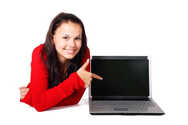 A smiling woman in a red shirt pointing at a blank laptop screen