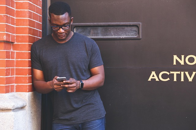 A man leaning against a wall while looking at his smartphone