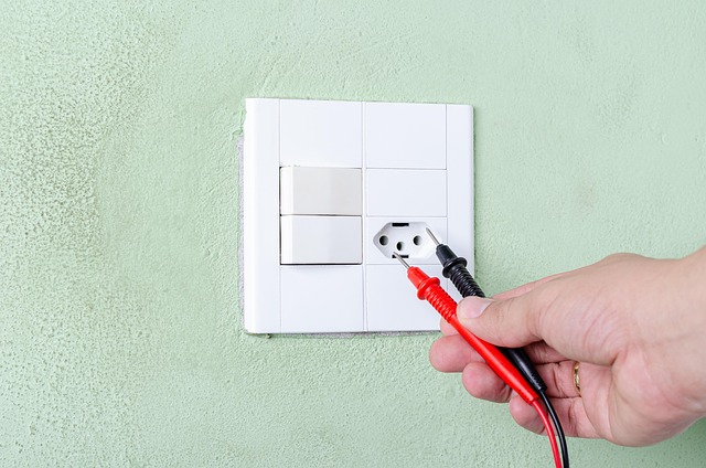 A hand holding multimeter probes near an electrical outlet